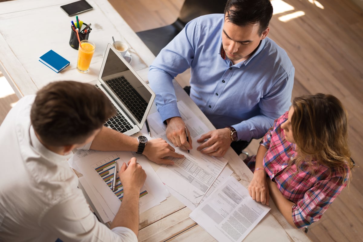 man and woman sitting across desk from man in business attire looking at financial documents