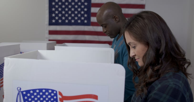 A woman and man standing next to each other at two voting booths separated by dividers.