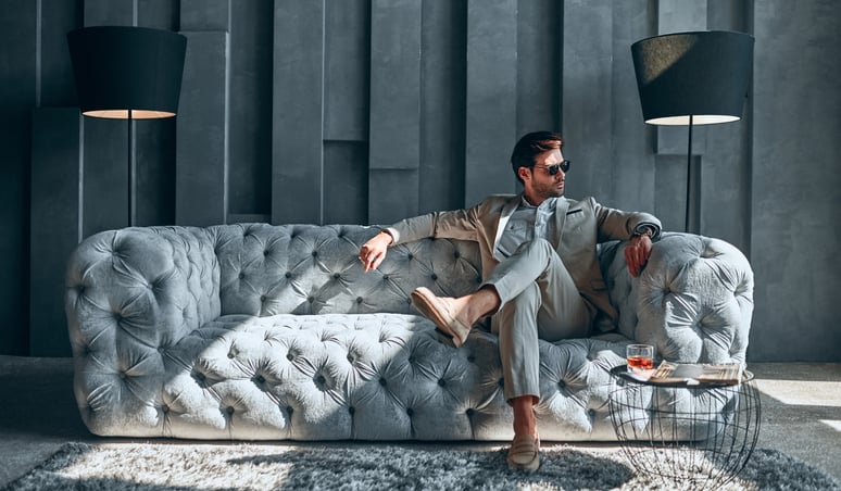 A stylishly dressed man sitting on an expensive-looking couch in a lavishly decorated room.