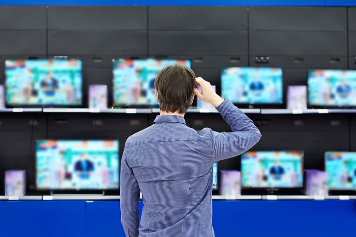 Un homme debout devant un mur de téléviseurs dans un magasin d'électronique.