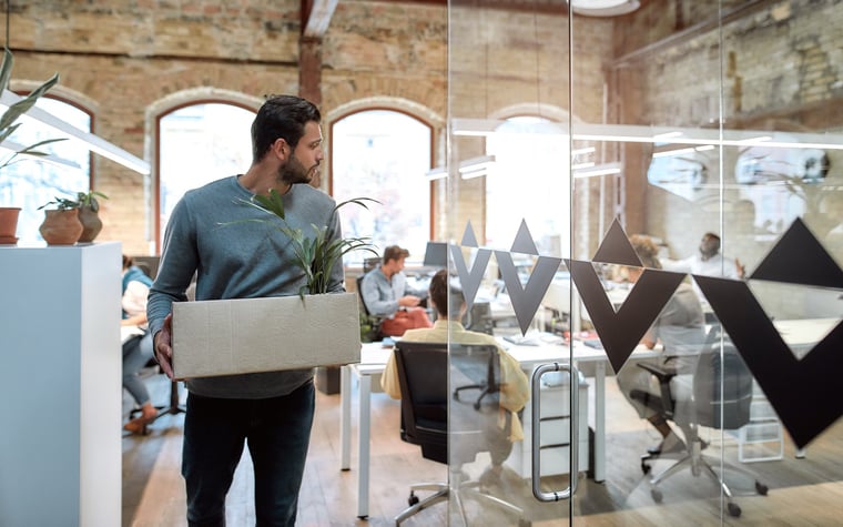 A man exits an office with a box of his things after leaving.