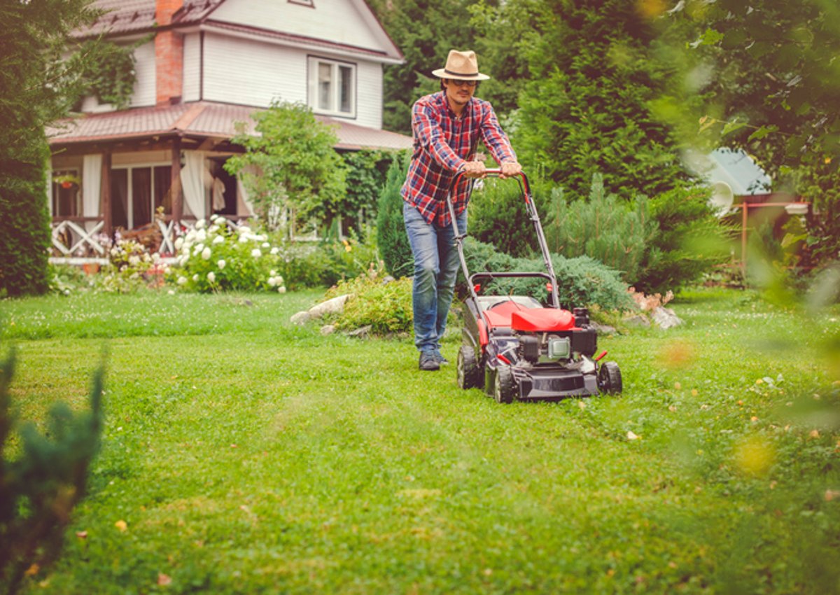 A man pushing a lawn mower with a house in the background.