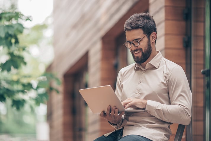 A man sitting in front of a brick building typing on a laptop.