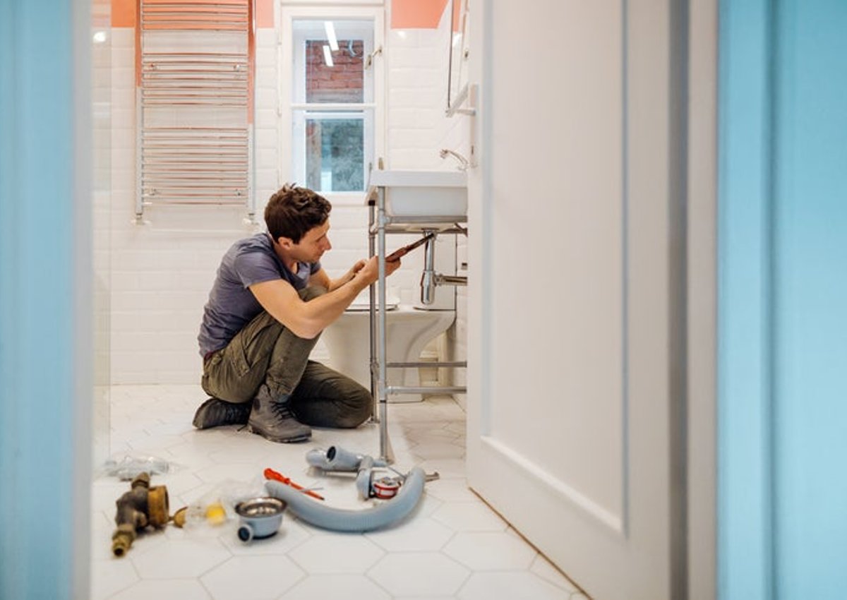 A man crouching on the floor next to tools while repairing a bathroom sink.
