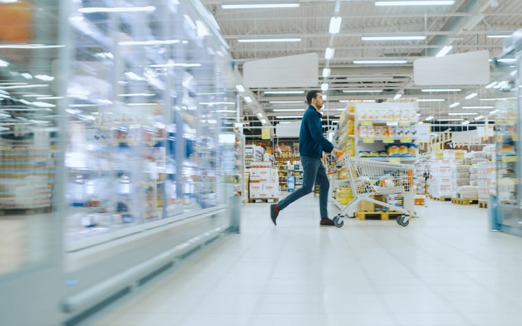 A man pushing a shopping cart through a warehouse store aisle.