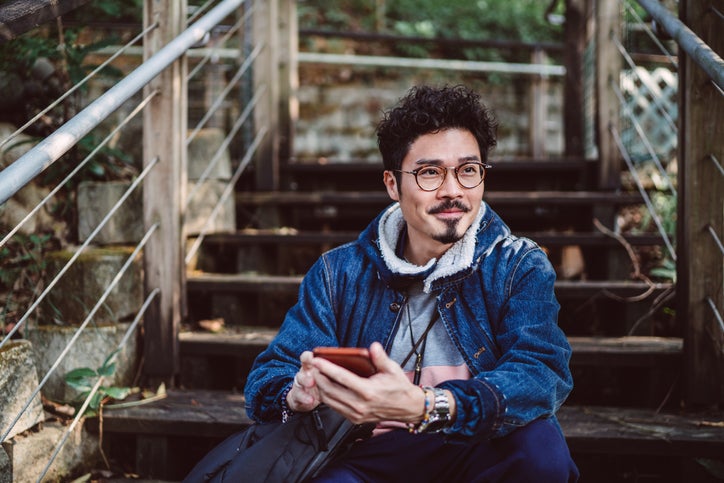 A man sitting on stairs in a park and holding a cell phone in his hand.