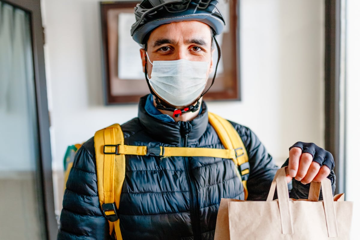 A man wearing a medical mask and delivering a bag of food.