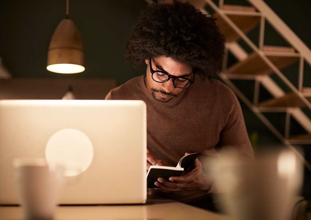 Man sitting with laptop and notebook late at night.