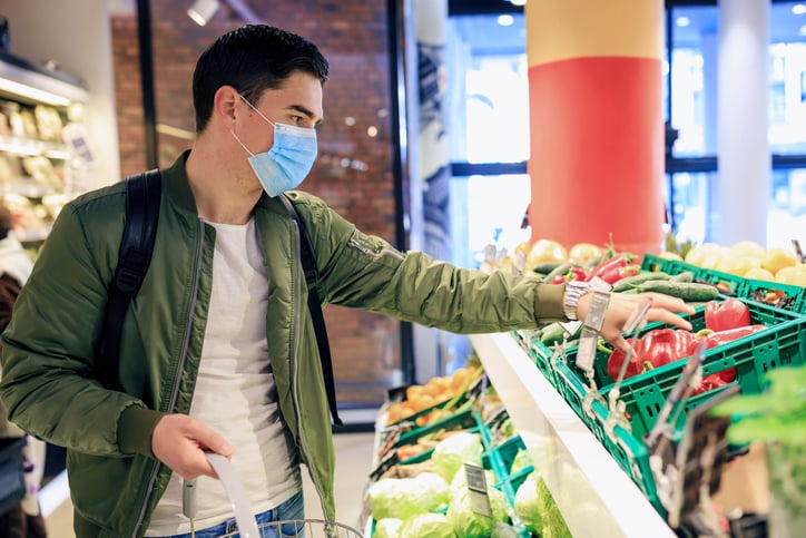A young man wearing a medical mask while shopping for produce at a grocery store.