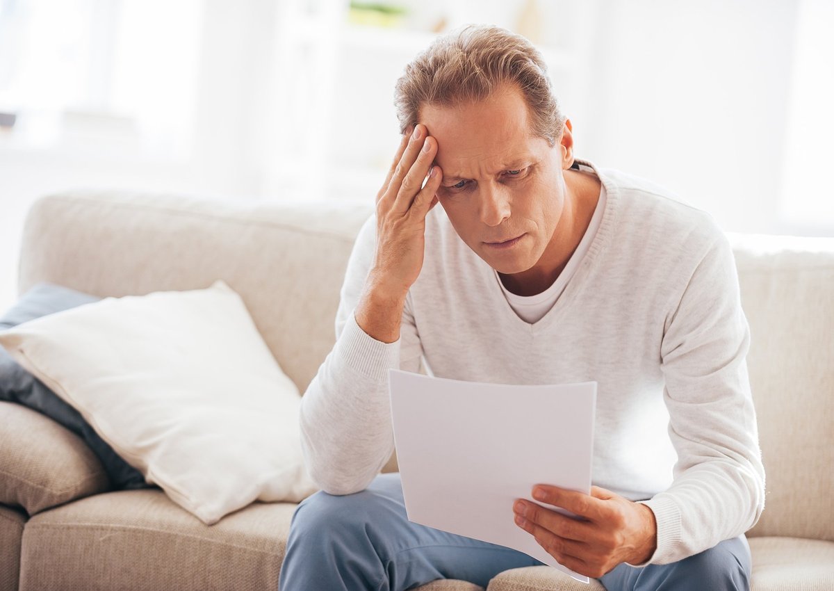 An adult man who rubs his temple while looking at a document.