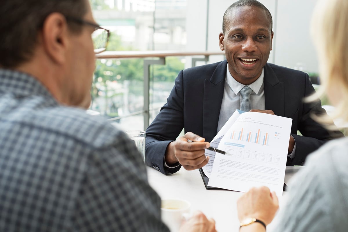 mature man and woman sitting at desk talking to man in business suit
