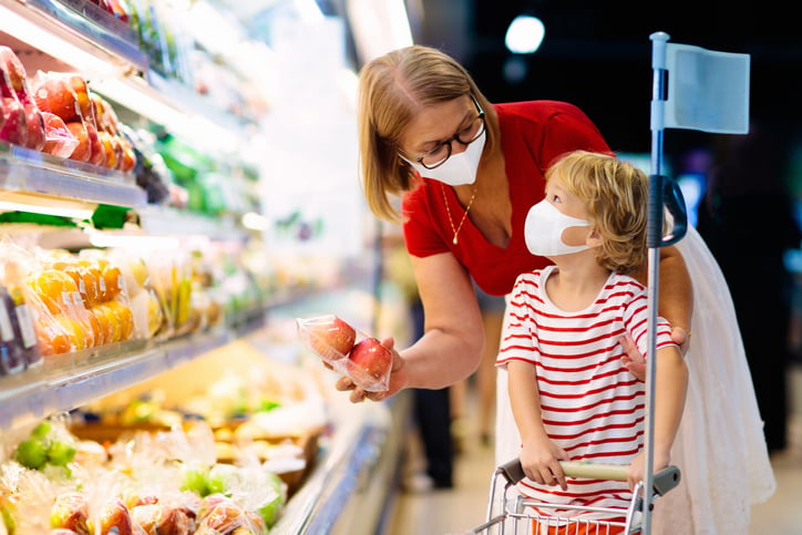 A mom and her young child shopping for fruit while wearing masks in a grocery store.