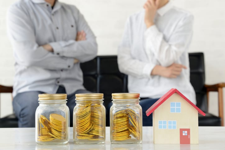 Two men blurred in background look at jars of coins and a small house