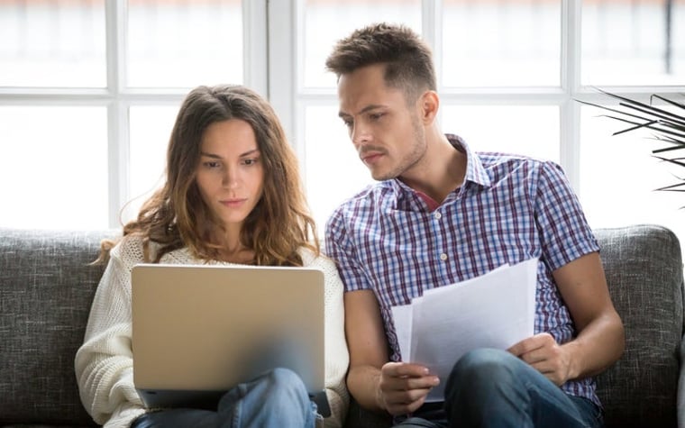 A couple looking worried about money, with a laptop and bills.