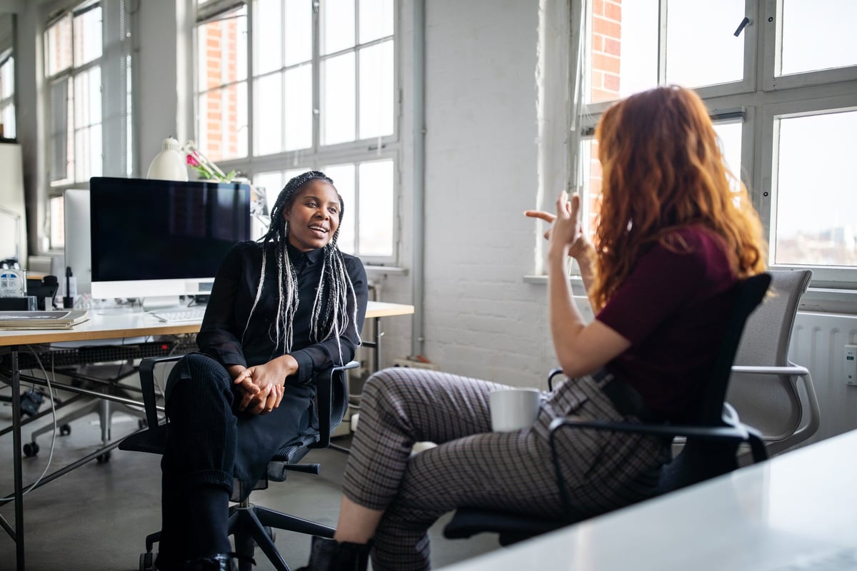 Two office employees chatting with each other from their desks.