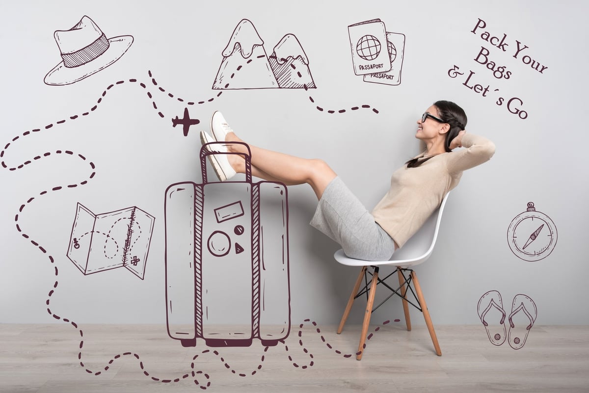Woman sitting in front of travel pictures with sign saying "pack your bags & let's go"