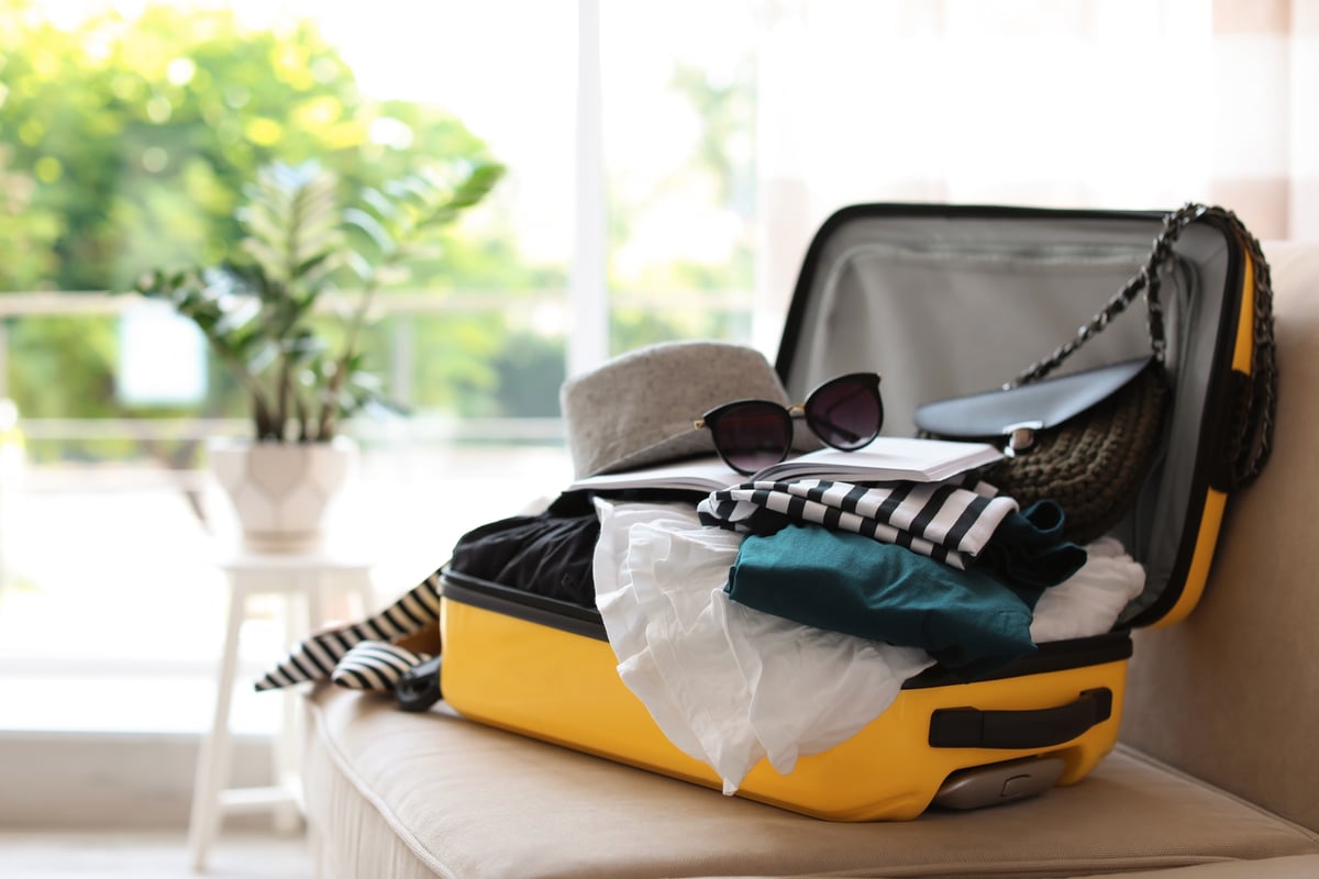 A suitcase packed with clothes sitting open in front of a sunny window.
