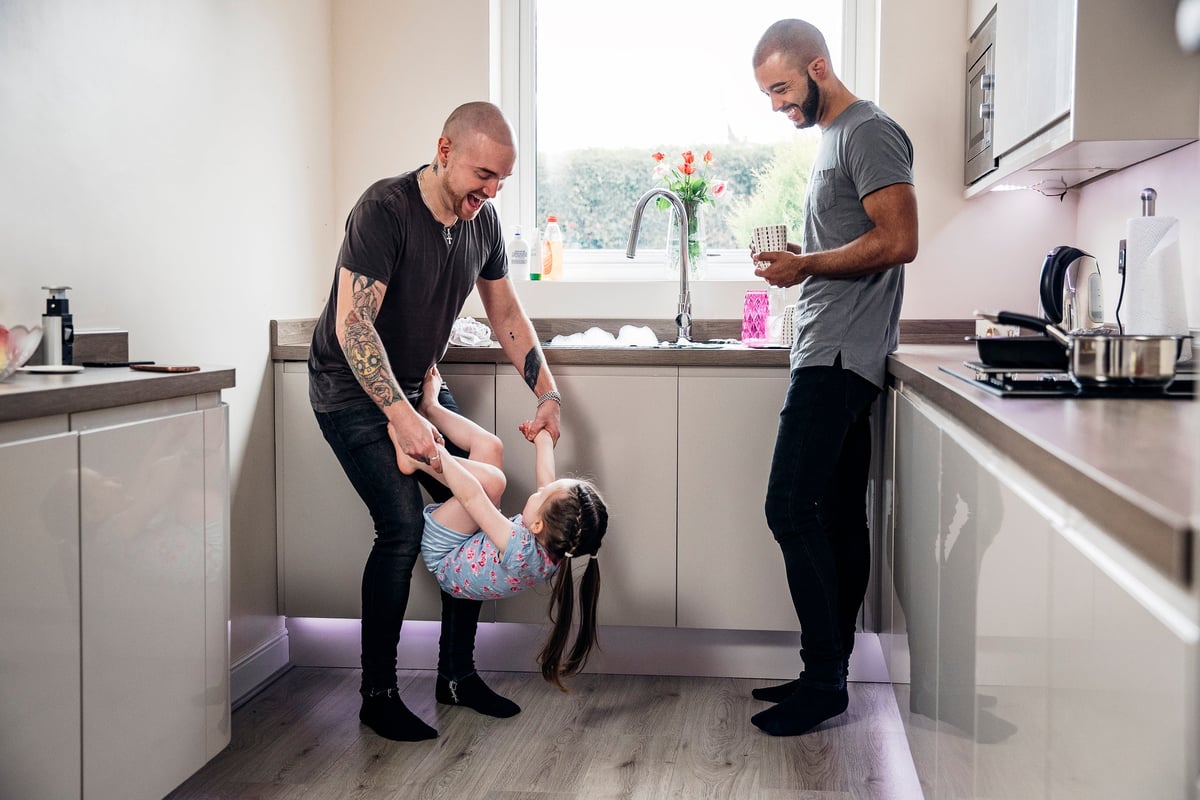 Two parents playing in the kitchen with their young child.