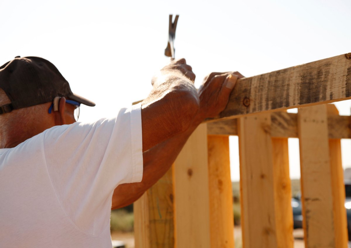 A person hammering nails into a new wooden fence.