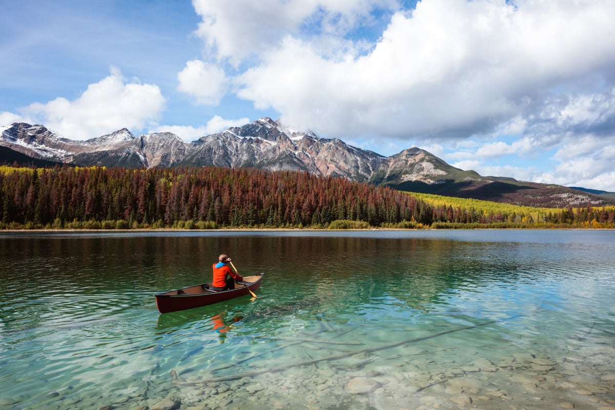 A person paddling a canoe across a clear blue lake surrounded by mountains in Canada.