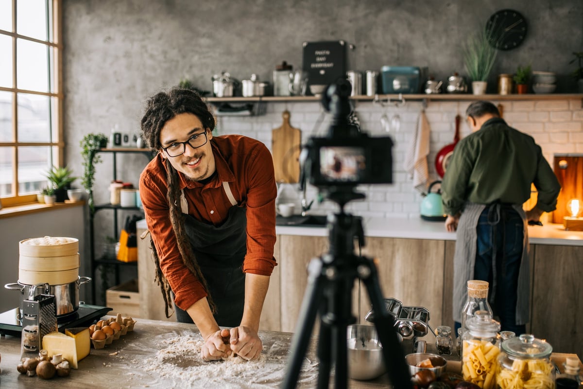 A person cooking in a nice kitchen while recording with a camera on a tripod.
