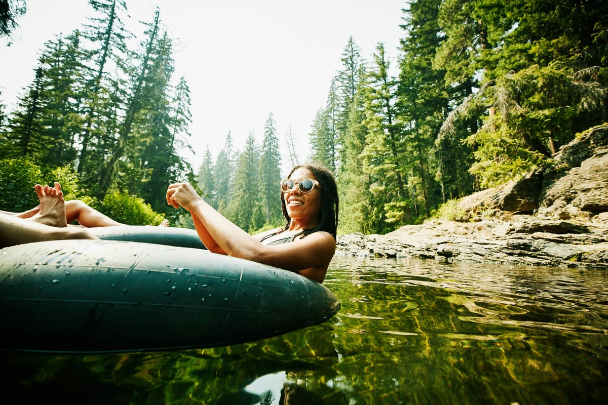 A person relaxing and floating in a tube down a river surrounded by tall trees.