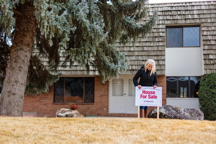 A person putting a House for Sale sign in the front lawn of their property.