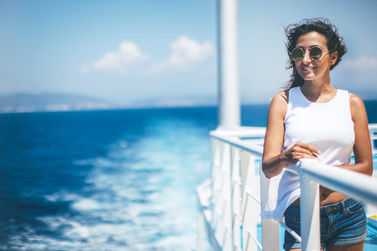 A smiling person standing at the railing of a cruise ship.