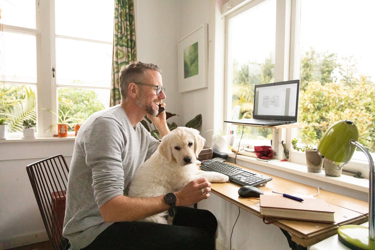 A person talking on the phone while sitting at a home office desk with a puppy in their lap.