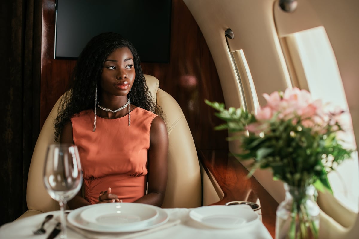 A person looking out the window while sitting at a table set with white linen and flowers on a private plane.