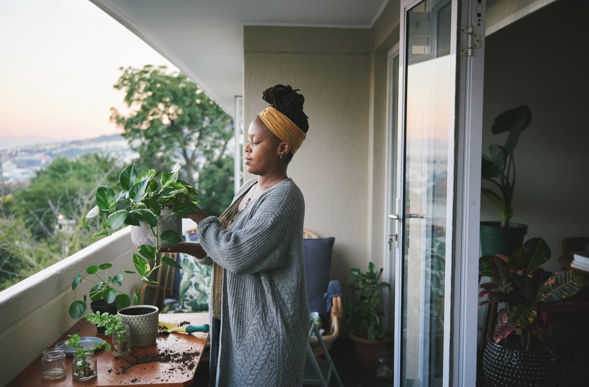 A person standing on a balcony and taking care of houseplants.