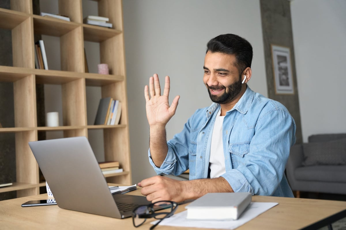 A person working at a desk at home and waving on a video call.