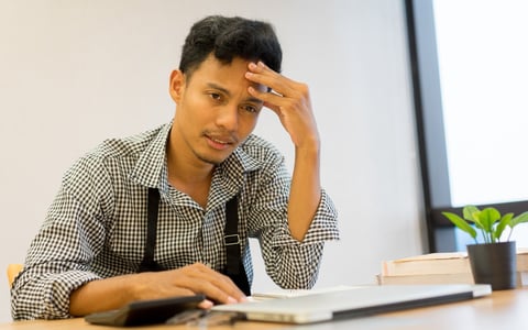 Dismayed man sitting at a desk with his hand on his forehead.
