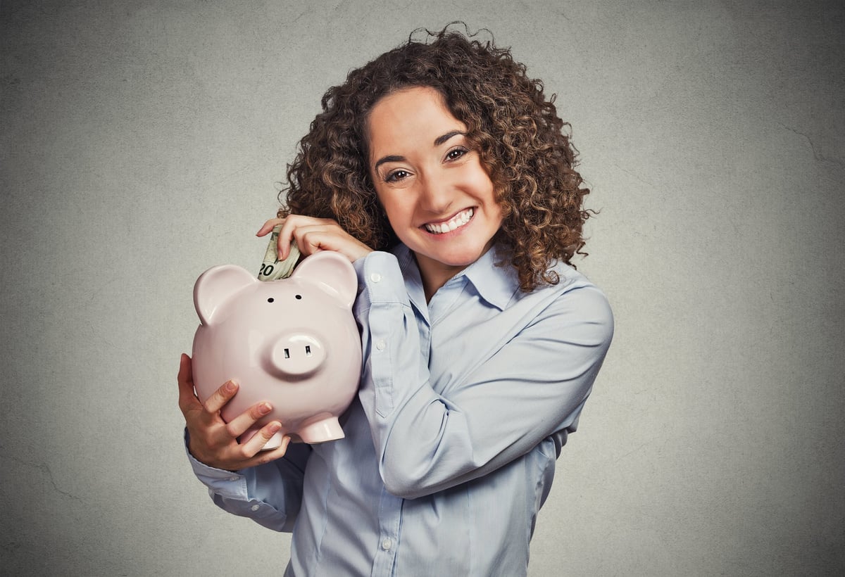 A smiling woman putting money into a piggy bank.