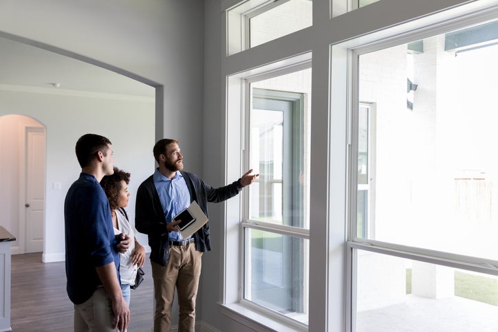 A realtor guiding a client through an empty house and pointing out the window.