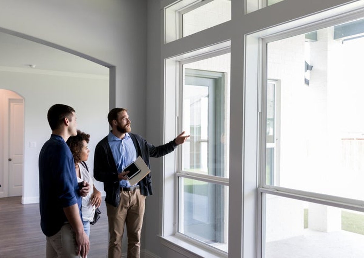 A realtor walking his clients through an empty house and pointing out the window.