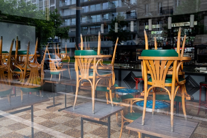 Chairs stacked on top of tables in an empty restaurant window.