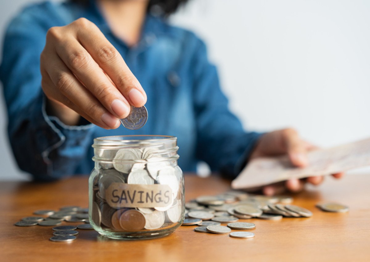 A woman puts a coin in a jar with a label "savings."