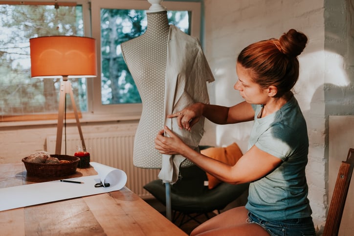 A seamstress holding up a piece of cloth to a body form in her home studio.