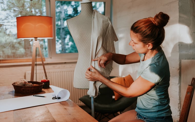 A seamstress holds a piece of fabric on a body shape in her home studio.