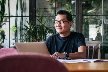 A smiling man working on a laptop in a room full of plants.