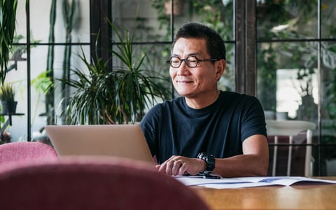 A smiling man working on a laptop in a room full of plants.