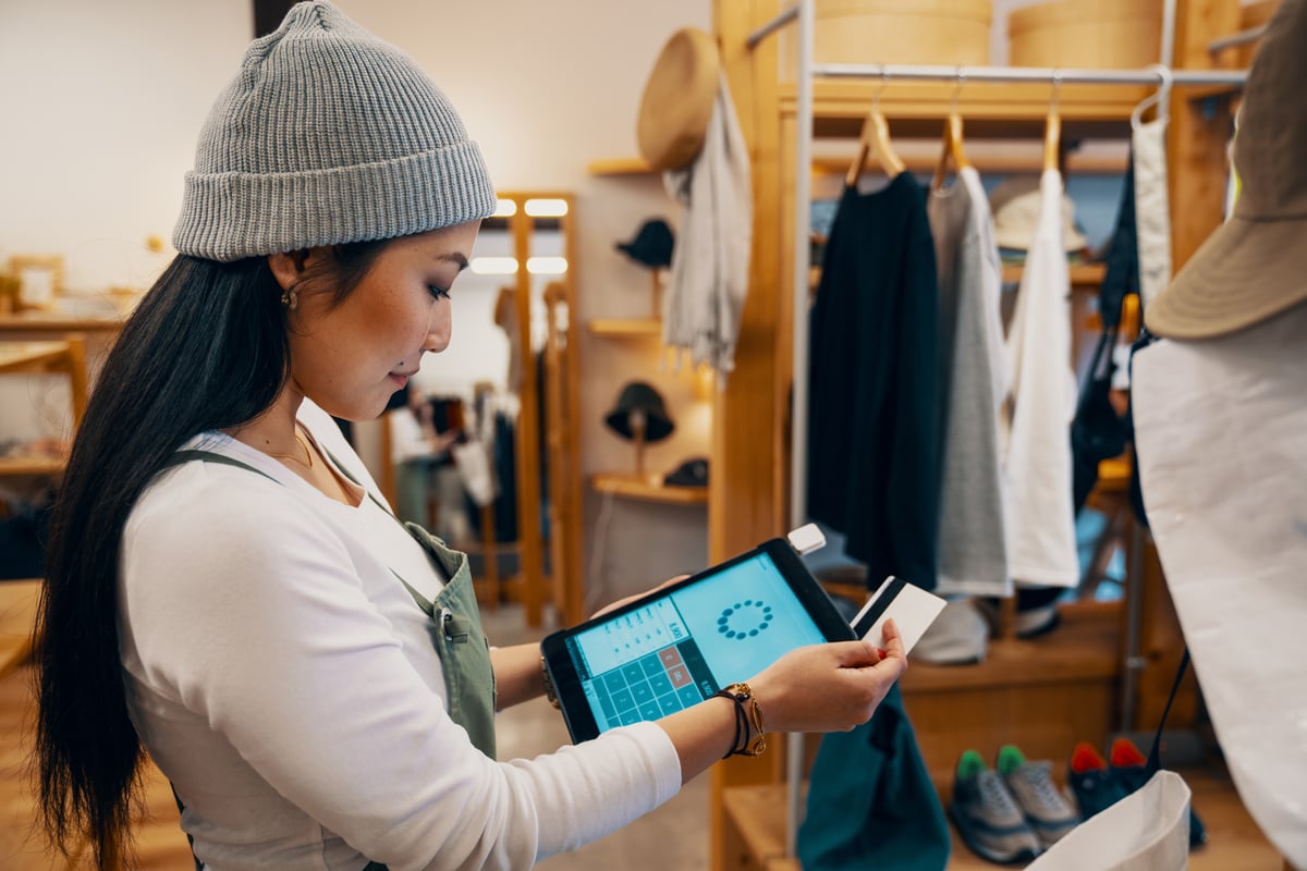 A female clerk at a clothing store swiping a credit card on a payment tablet.