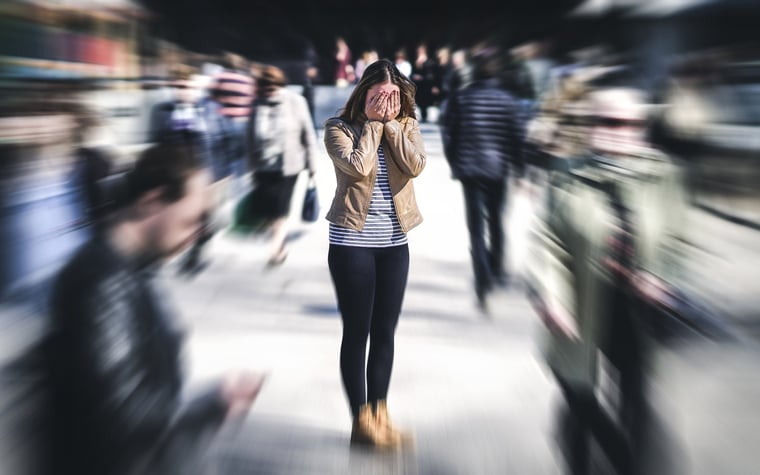 Stressed young woman covering her face with her hands in a busy crowd.