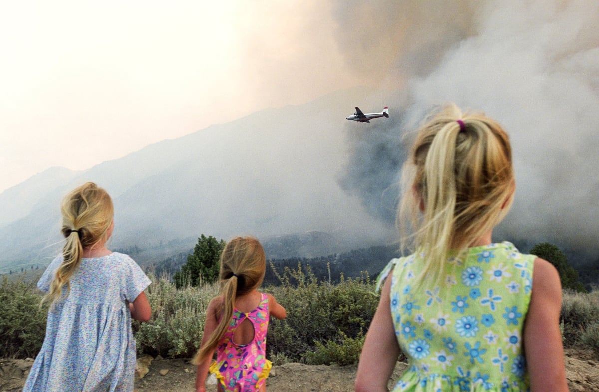 Three young children watching a firefighting plane fly over wildfire smoke.