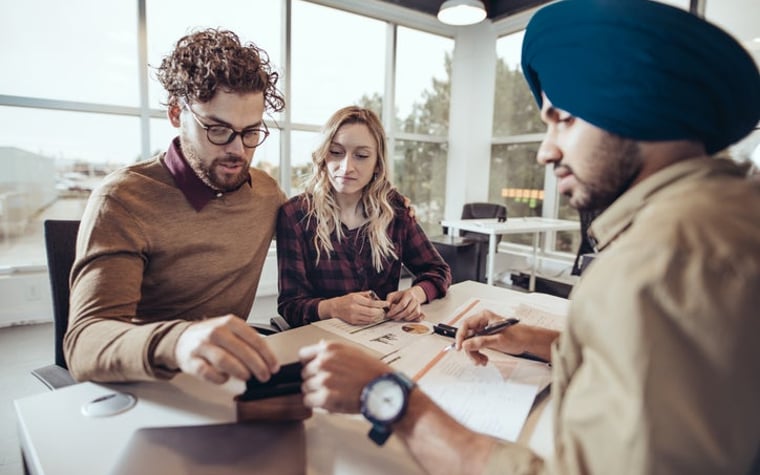 A man and woman meeting with a financial professional at his desk in an office.