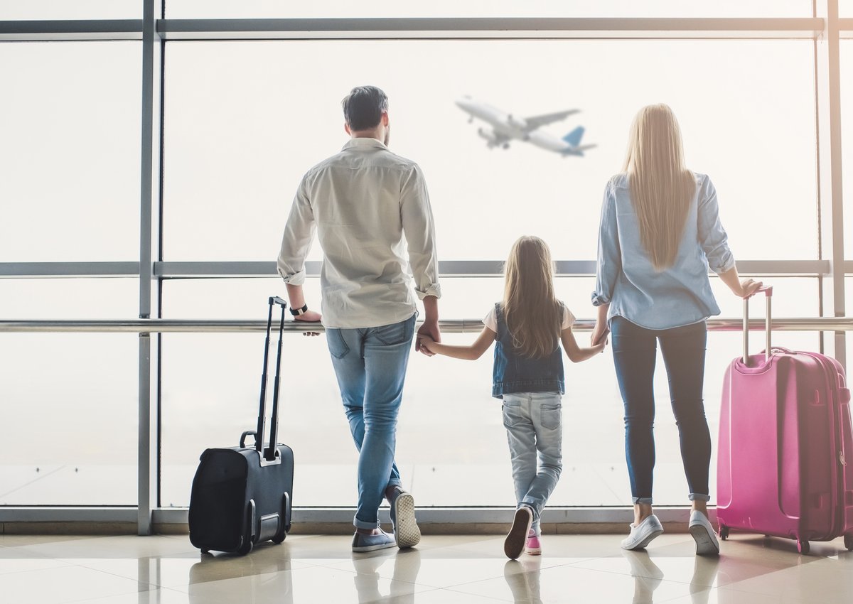 man, woman, and girl holding hands and watching airplane take off