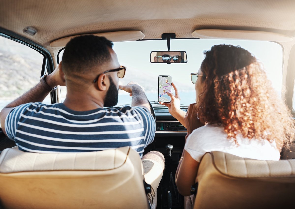 Two people driving in a car on a sunny day while looking up directions on a smartphone.