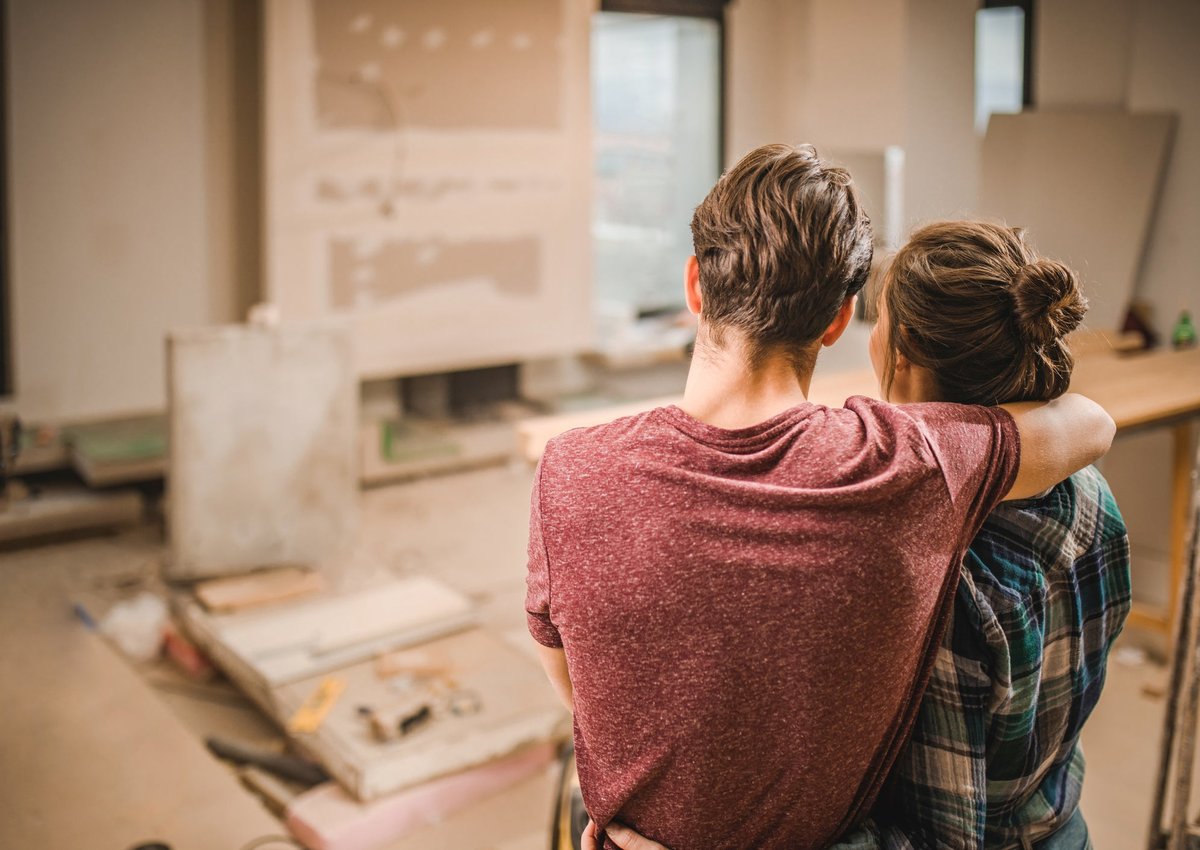 Two people with their arms around each other looking at their living room under construction.
