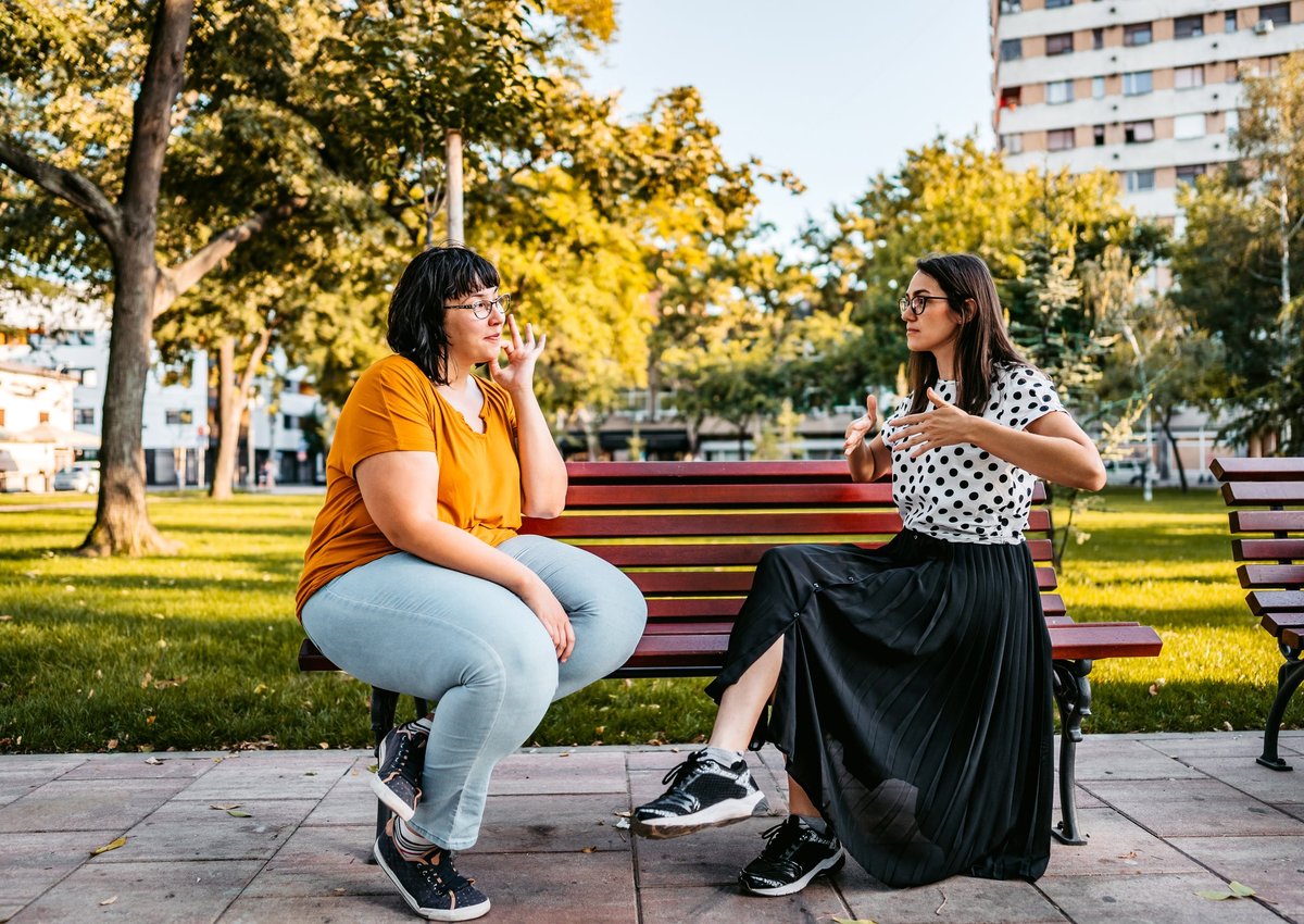 Two people sitting on a park bench and speaking in sign language.